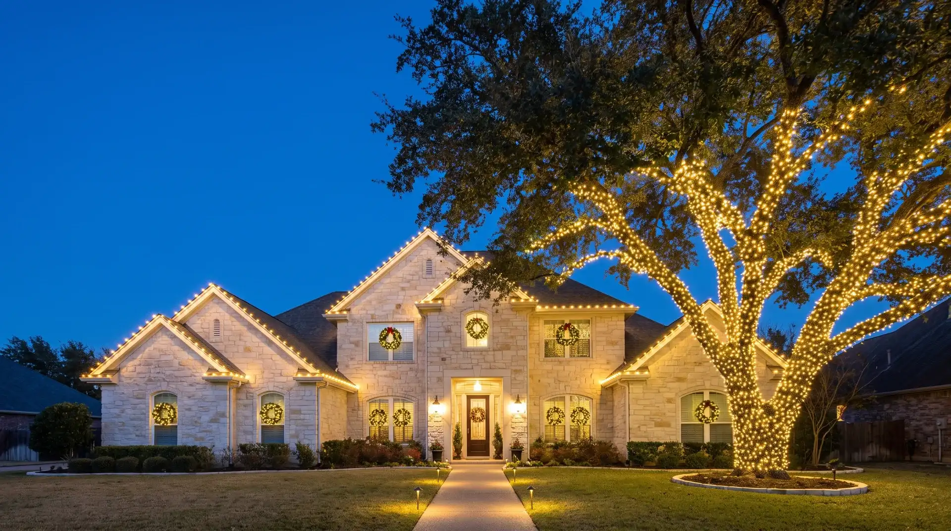 Two-story Austin home with professionally installed warm-white Christmas lights on the roofline and wrapped live oak