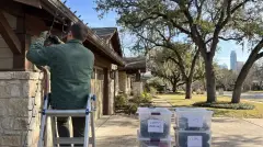 Installer taking down Christmas lights from a craftsman home under live oaks in Austin, TX for labeled storage