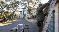 Installer taking down Christmas lights from a wooded hillside home in West Lake Hills, TX for labeled storage