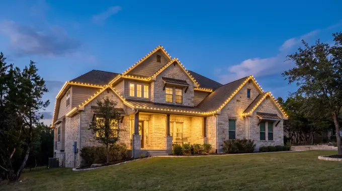 Custom-fit warm-white C9 Christmas lights outlining the roofline of a limestone Hill Country home in Cedar Park, TX