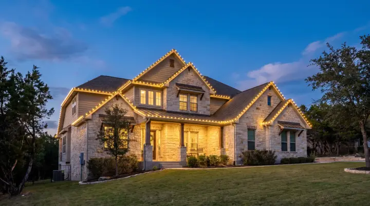 Custom-fit warm-white C9 Christmas lights outlining the roofline of a limestone Hill Country home in Cedar Park, TX