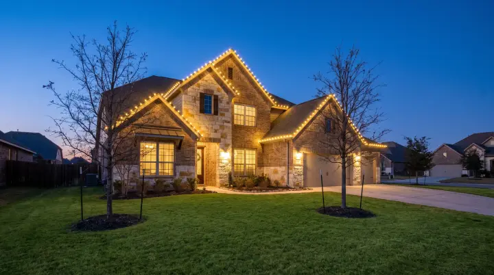 Custom-fit warm-white C9 Christmas lights outlining the roofline of a two-story brick home in Round Rock, TX