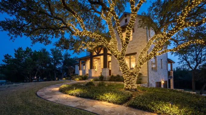 Live oak wrapped in Christmas lights with lit landscaping at a limestone Hill Country home in Cedar Park, TX