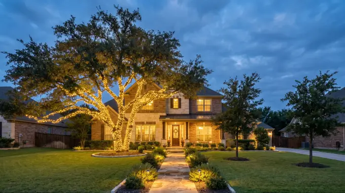 Live oak wrapped in Christmas lights with lit landscaping at a two-story brick home in Round Rock, TX