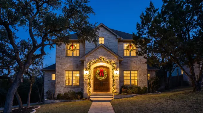 Pre-lit wreath and garland installed on the front entry of a limestone Hill Country home in Cedar Park, TX