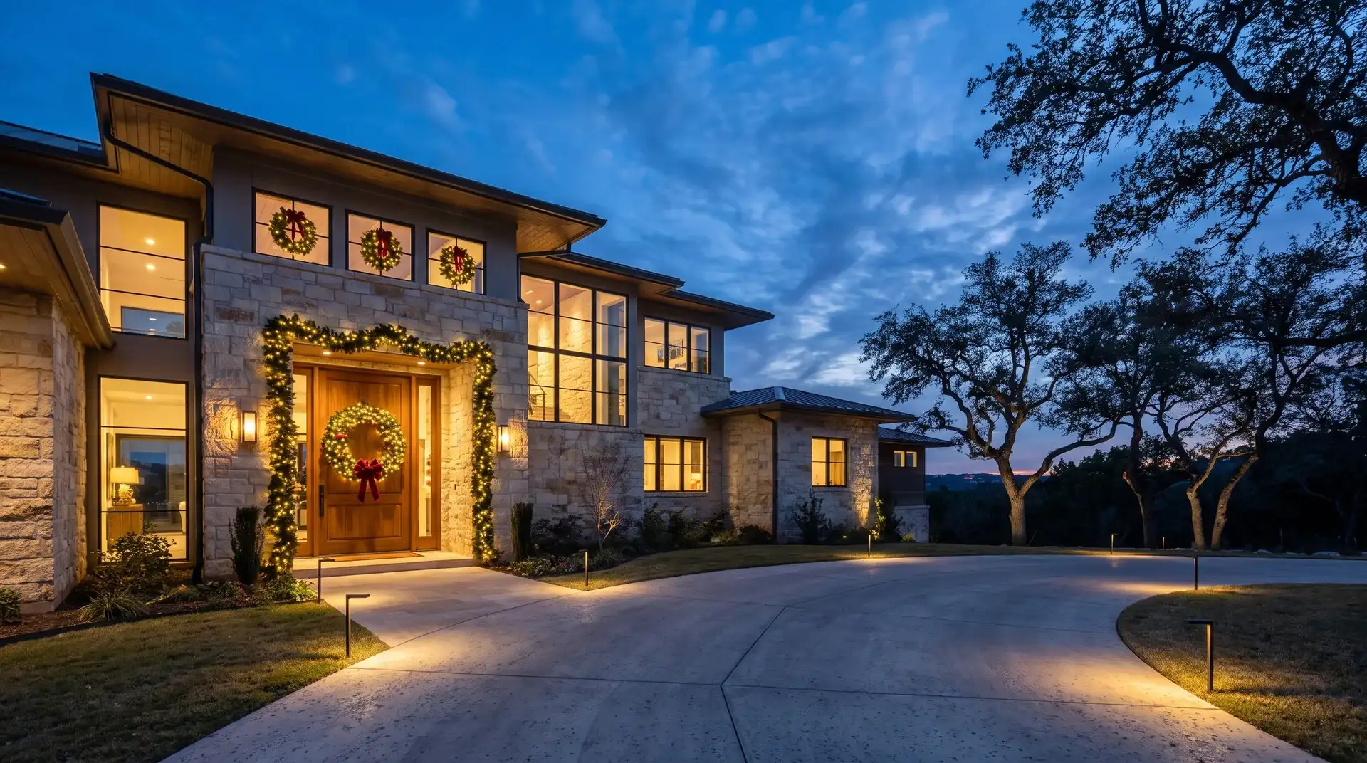 Pre-lit wreath and garland installed on the front entry of a wooded hillside home in West Lake Hills, TX